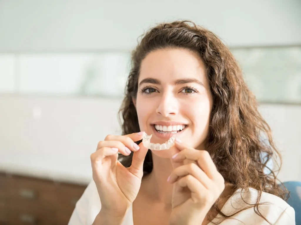 adult holds invisalign tray while she learns invisalign faqs
